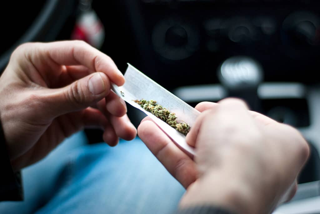 man making joint and a stash of marijuana in the car